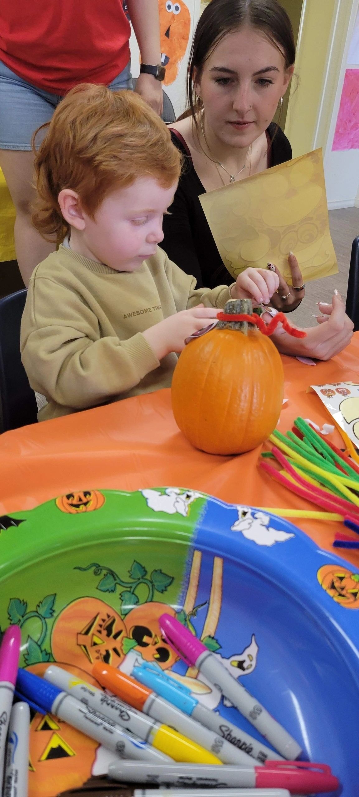 Child decorating pumpkin with adult helper