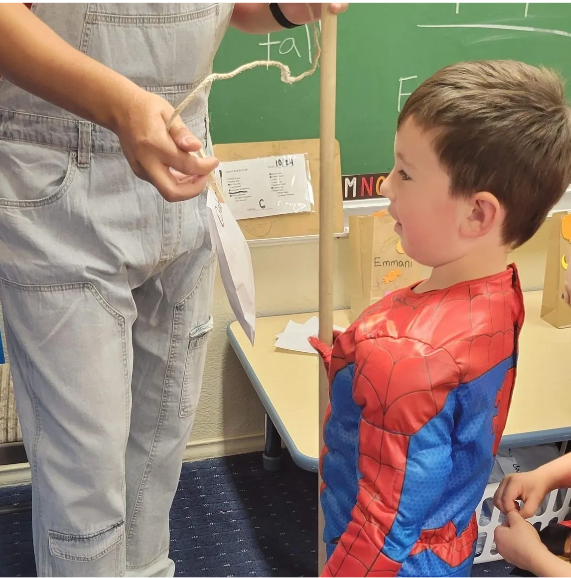 Child in Spider-Man costume with teacher in classroom
