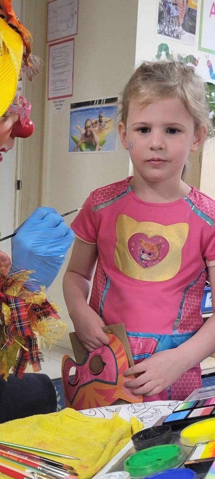 Child getting face painted by clown at school event