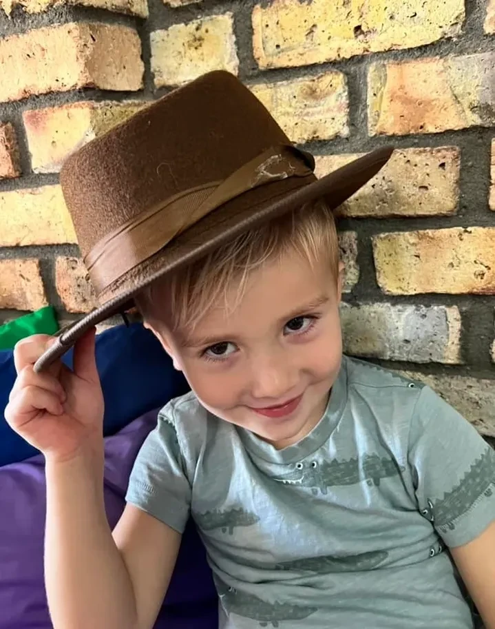Child in cowboy hat smiling against brick wall